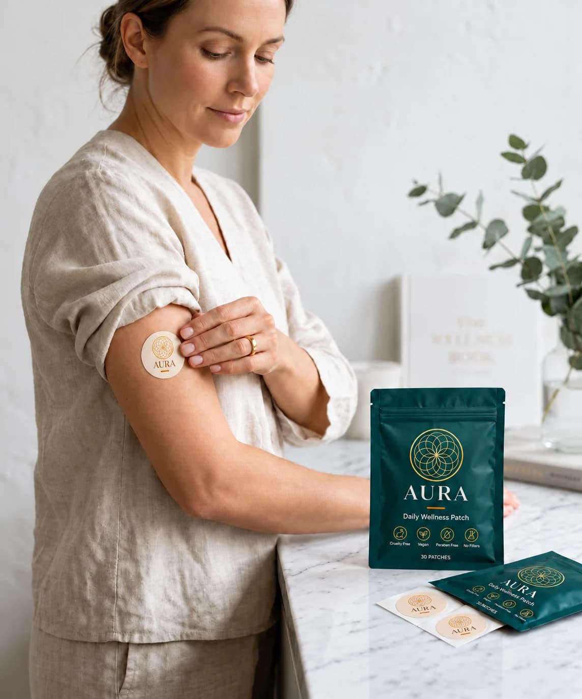 Woman applying the gold AURA patch beside the current teal Daily Wellness Patch pouch